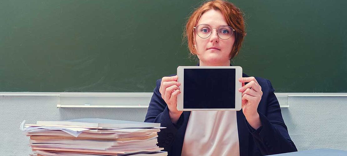 Lehrerin sitzt an einem Tisch mit einem Tablet in den Händen